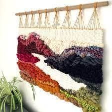 A woven tapestry is hanging on a wall next to a plant.