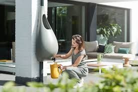 A woman is watering a plant with a watering can attached to a wall.