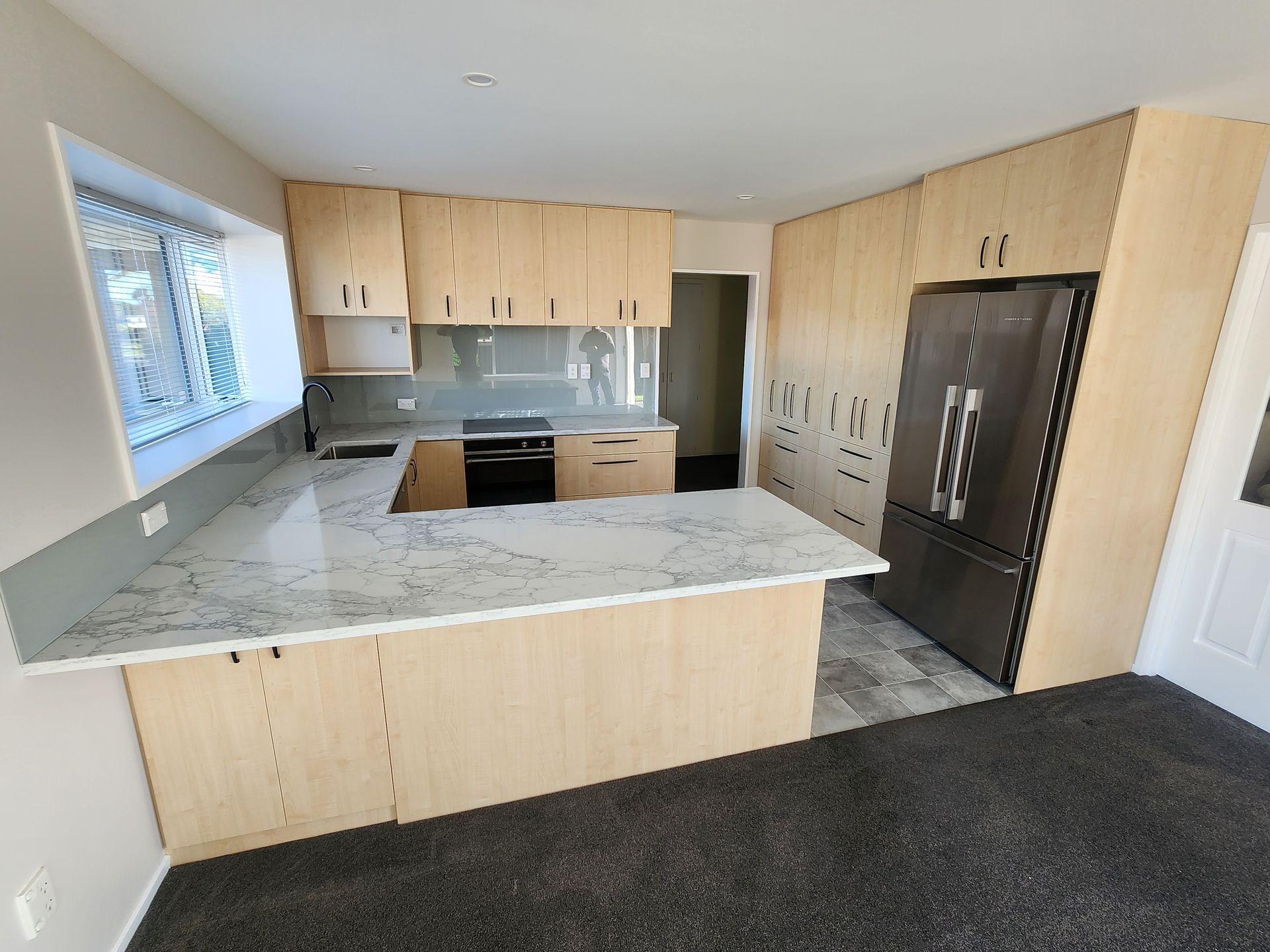 Modern kitchen with light wood cabinets, marble island, dark flooring, and stainless steel appliances