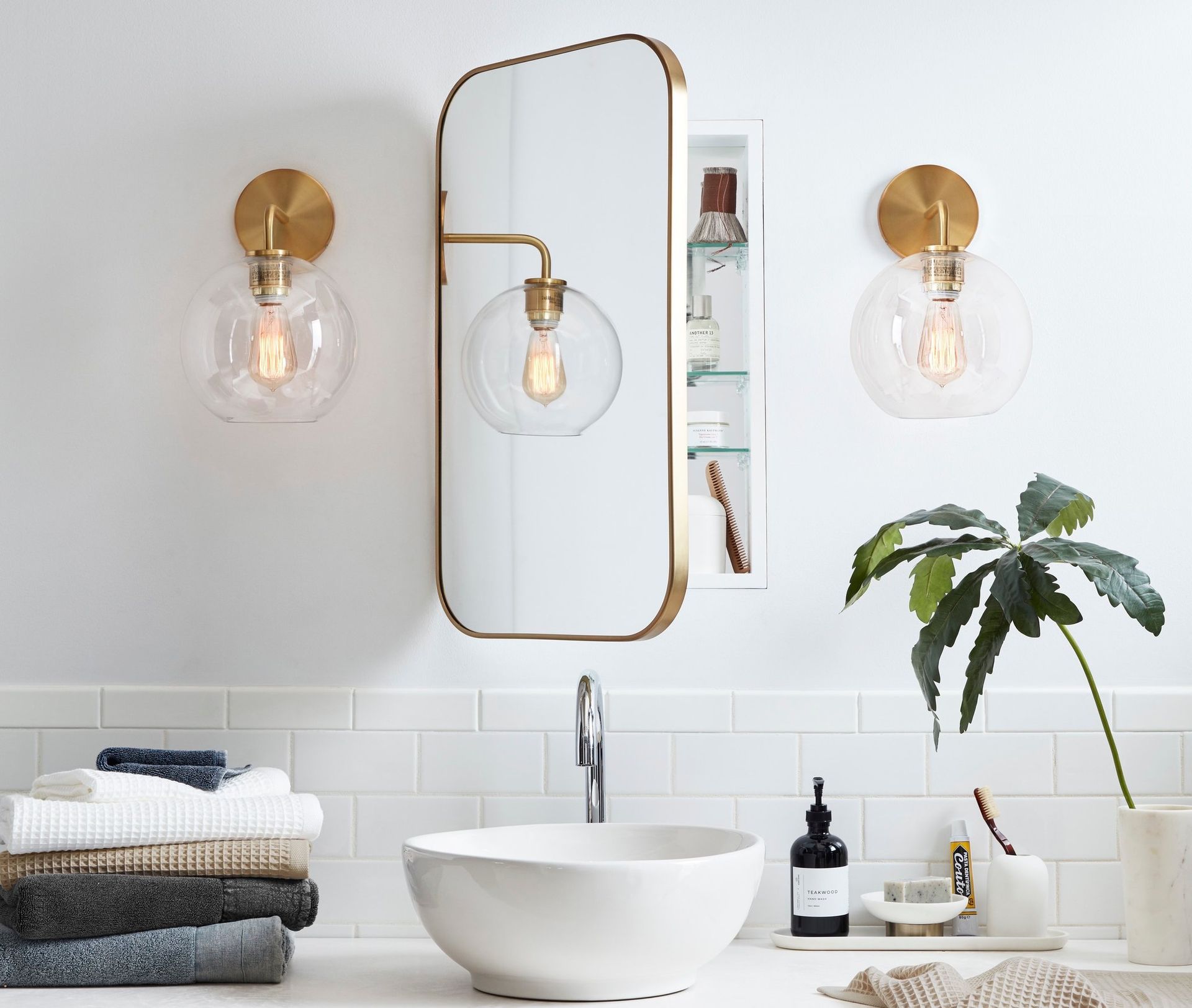 A bathroom with a sink , mirror , light fixtures and a plant.