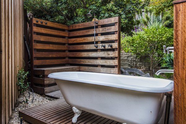 A bathtub is sitting on a wooden deck next to a wooden fence.
