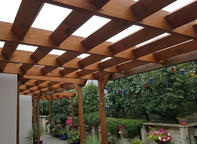 A wooden pergola with a clear roof is in a garden.