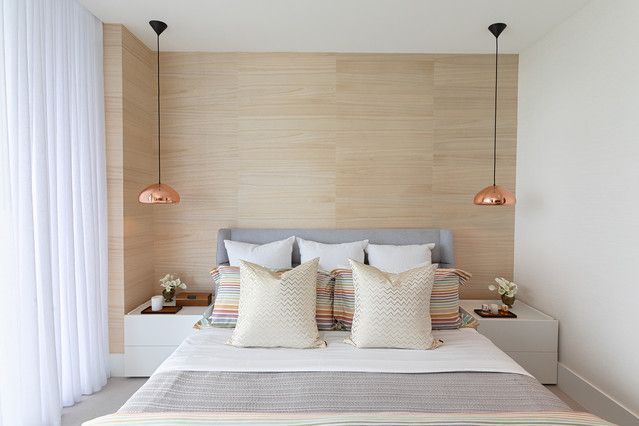 A bedroom with a bed , nightstands , lamps and a wooden wall.