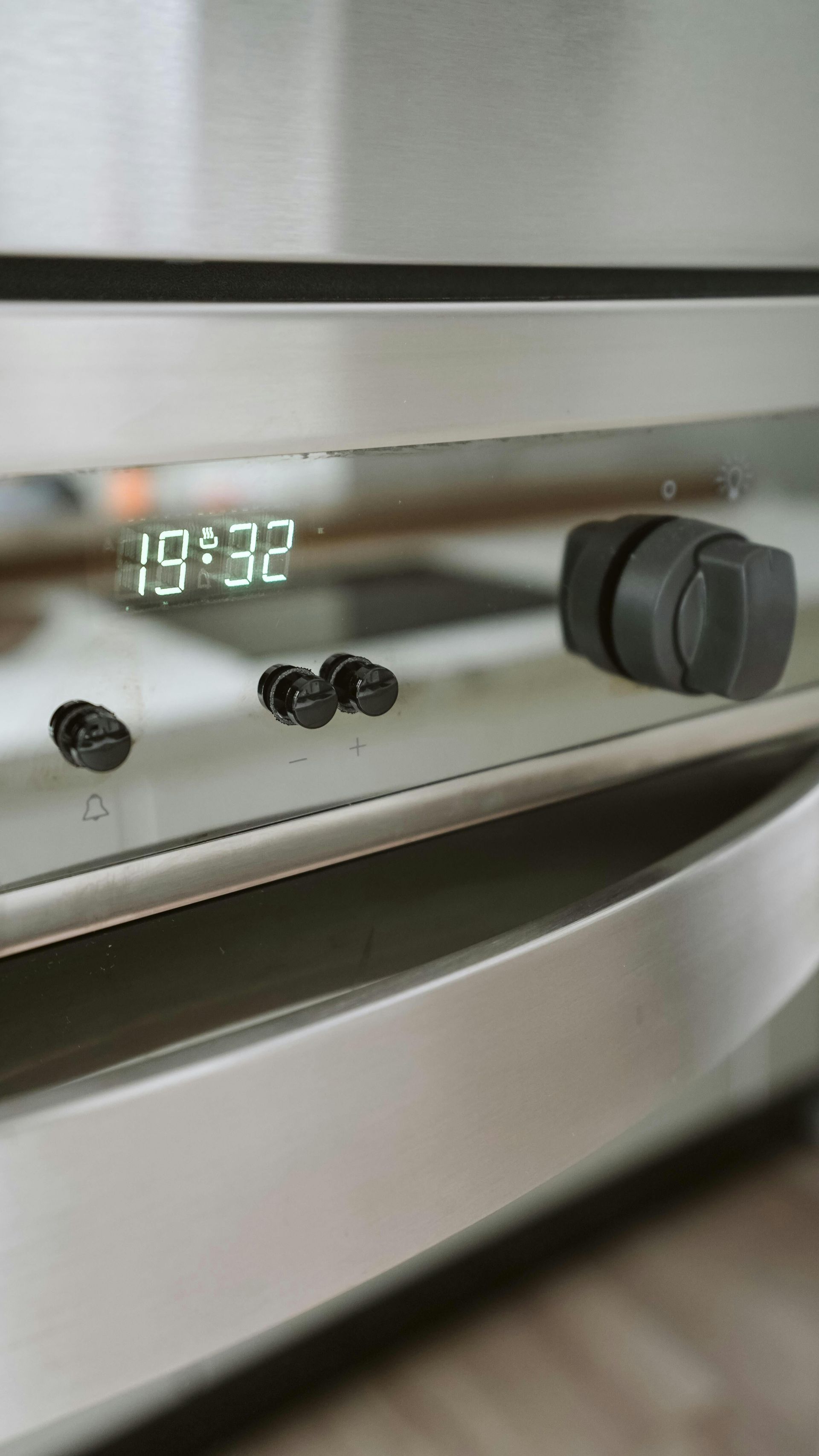 Close-up of a stainless steel oven control panel showing 19:32 and a black knob.