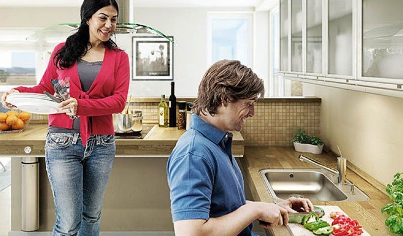 A woman is standing next to a man cutting vegetables in a kitchen.
