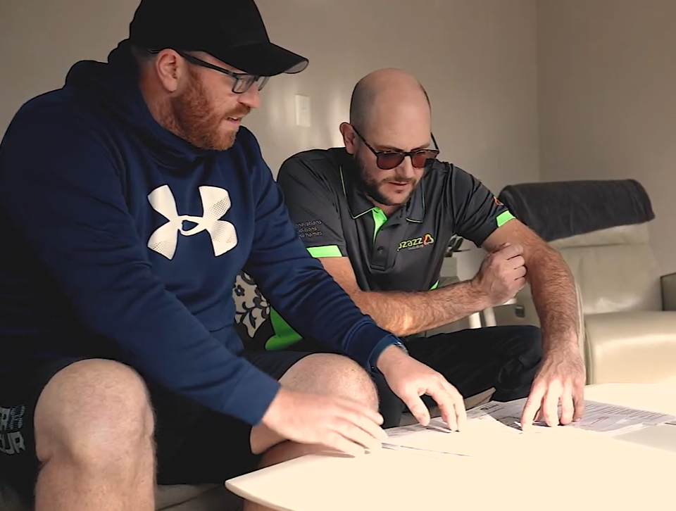 Two people lean over a table, reviewing documents together in an in-home consultation for a home renovation project.