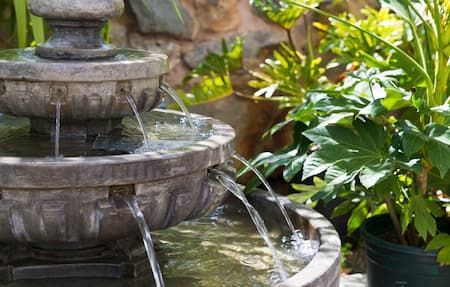 A fountain is surrounded by potted plants in a garden.