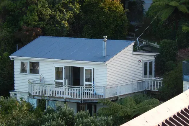 A white house with a blue roof is surrounded by trees