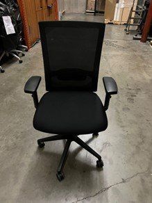 A black office chair is sitting on a concrete floor in a warehouse.