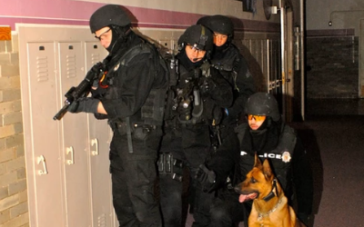Police officers with a German shepherd conducting a tactical operation at night beside a building
