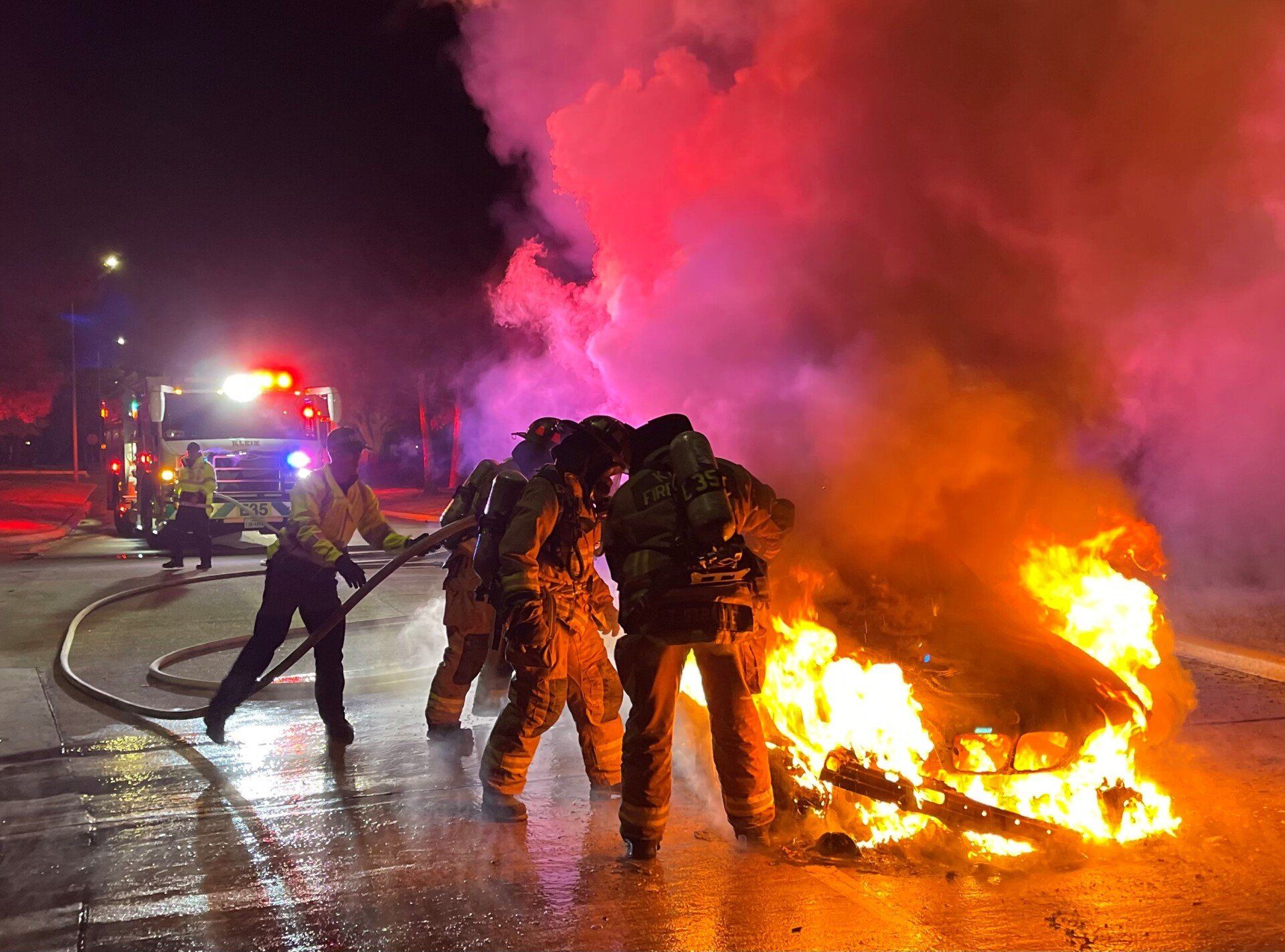 A group of firefighters are fighting a car fire.