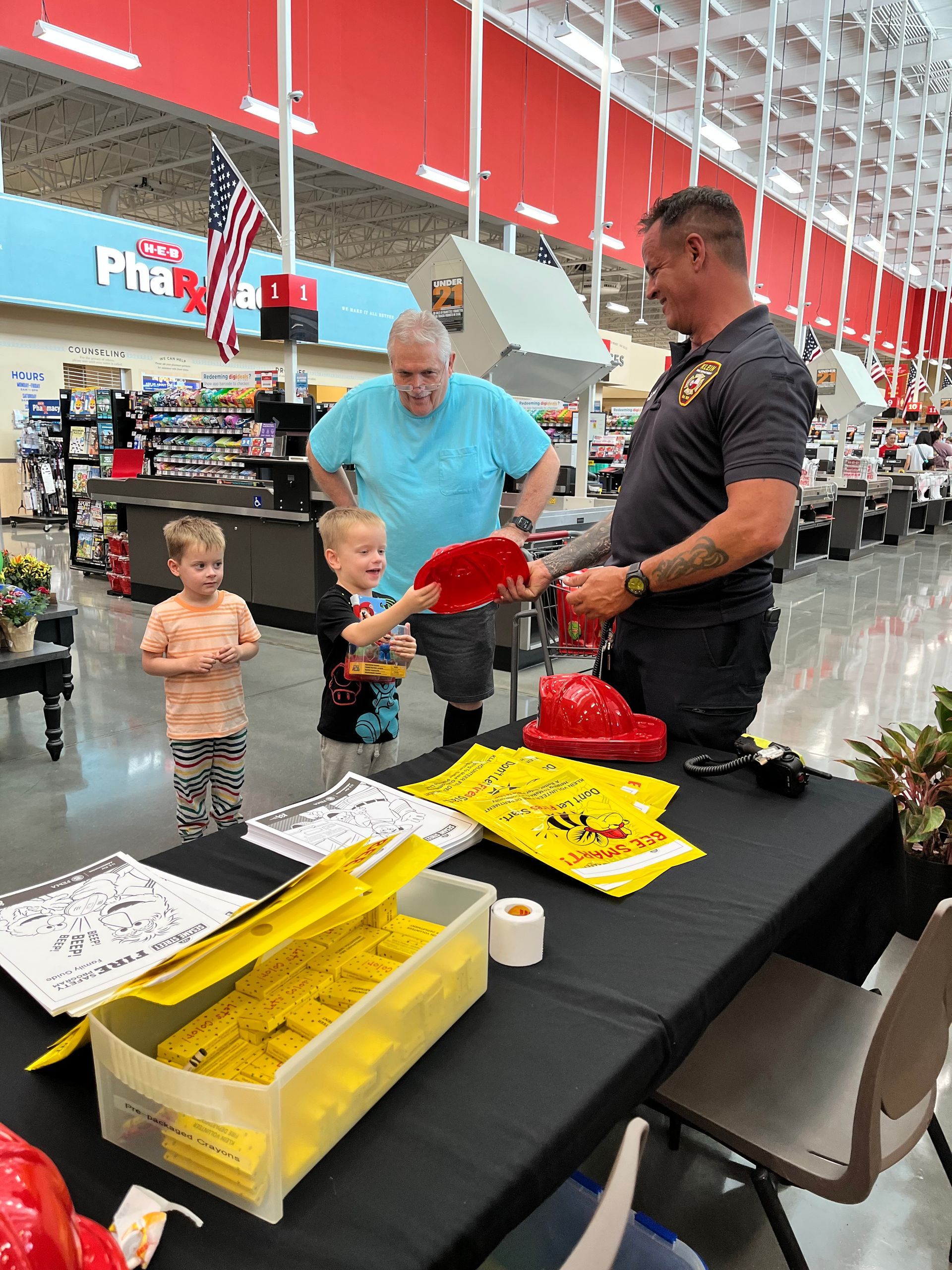 A fire fighter and two children are standing around a table in a store.
