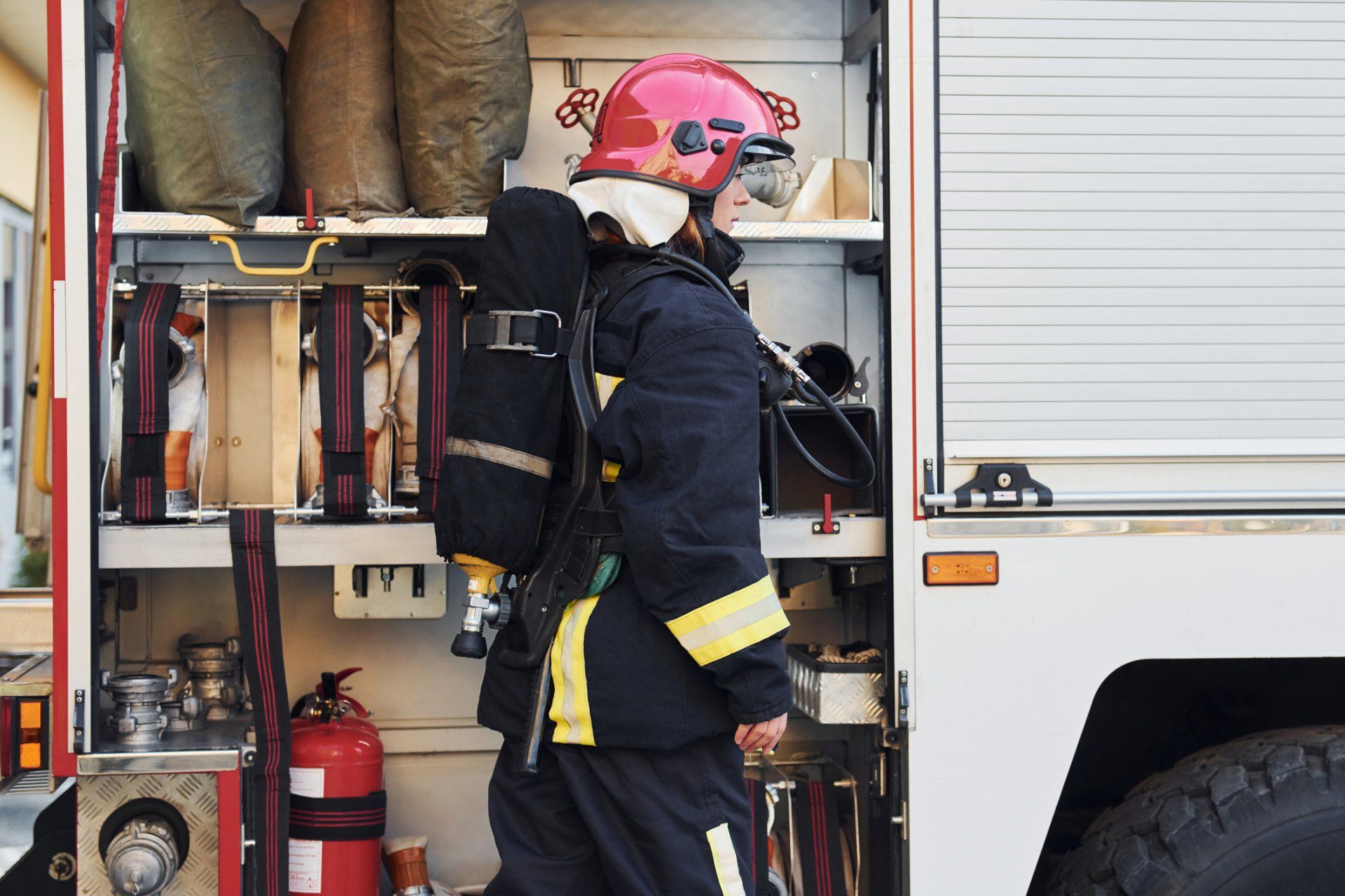 A fireman is standing in the back of a fire truck.