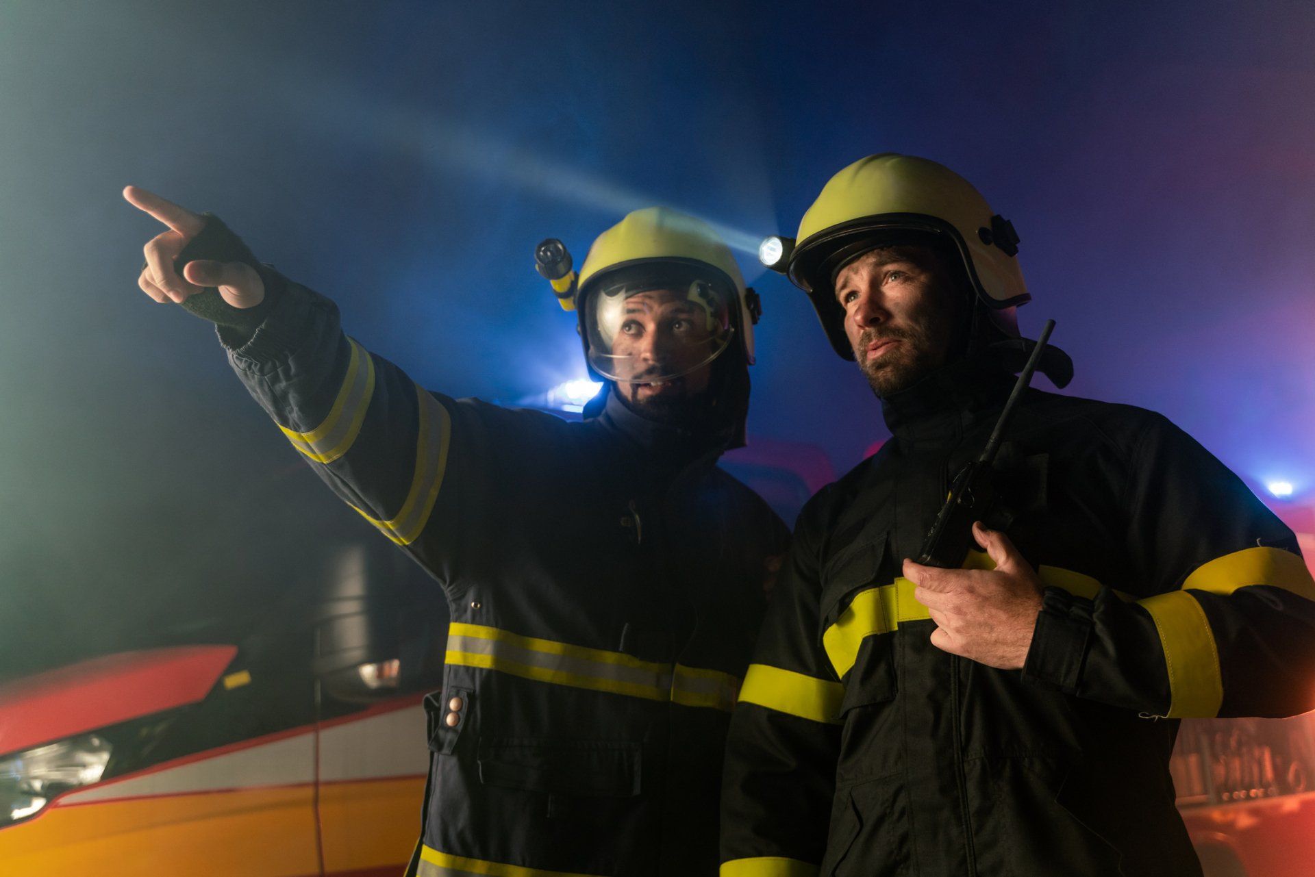 Two firefighters are standing next to each other and pointing at something.