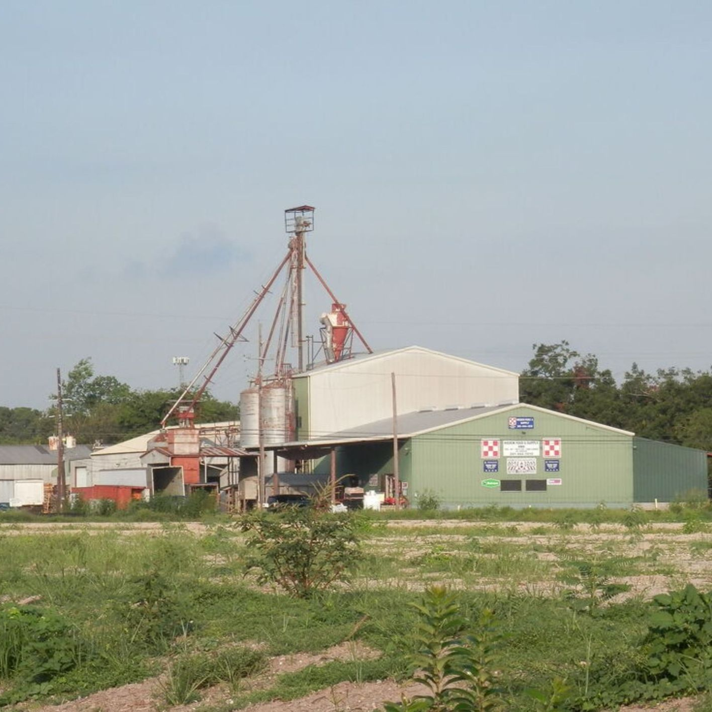 Industrial factory with tall metal silos and a green-roofed warehouse in a grassy field