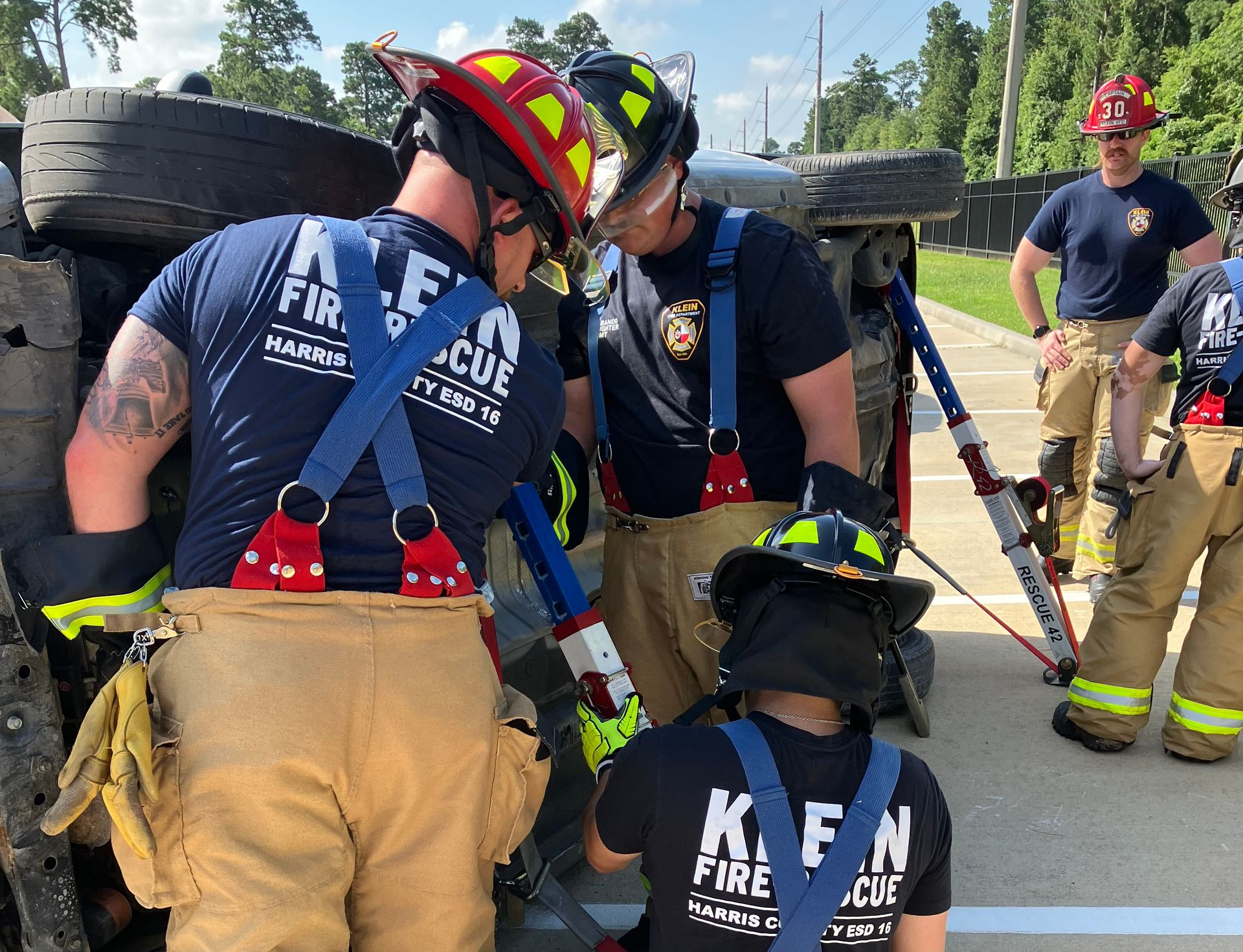 Firefighters in helmets and turnout gear work together around a tire near a road.