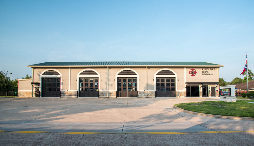 A large building with a maltese cross on it is sitting in the middle of a parking lot.