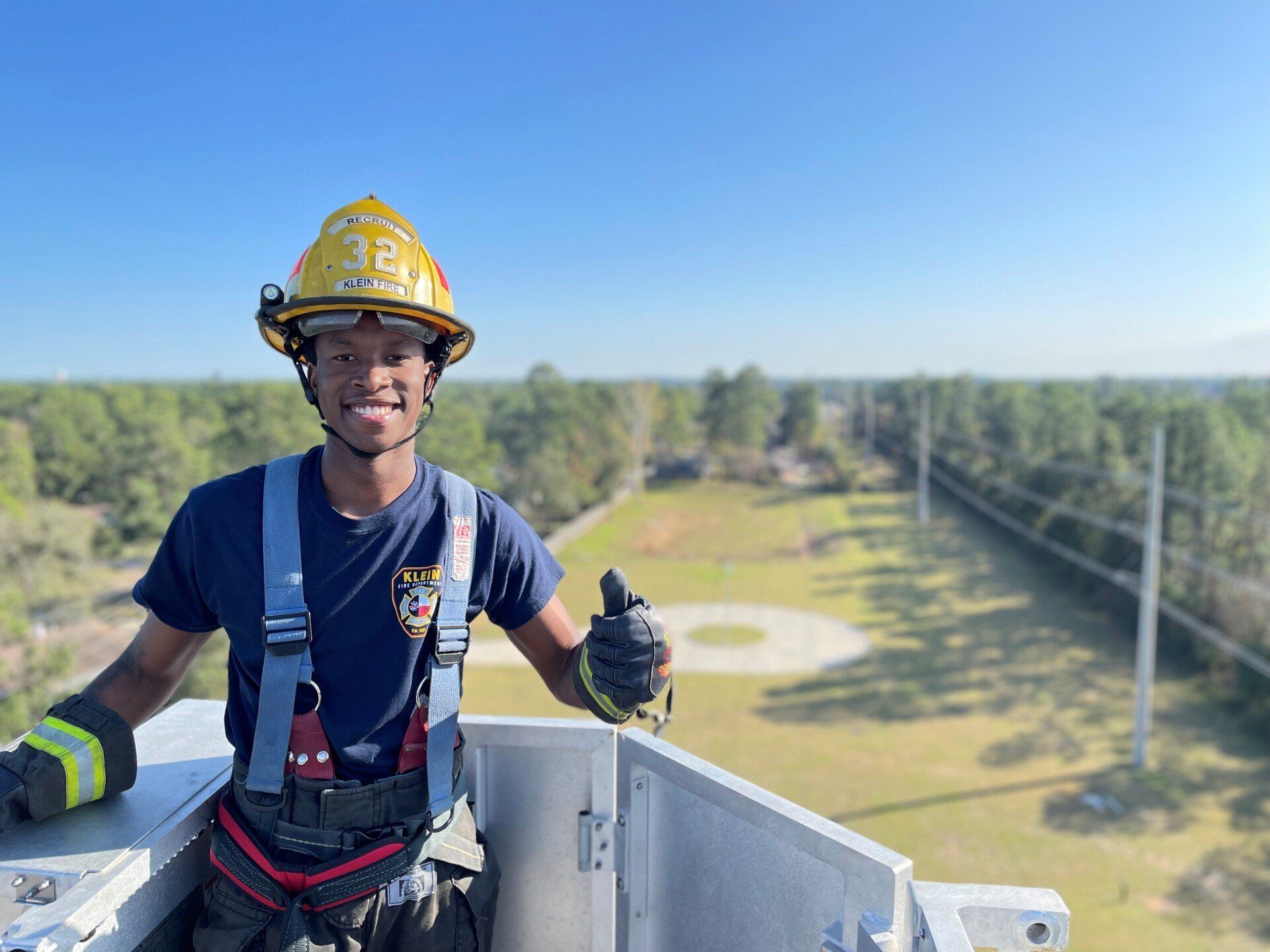 A man wearing a hard hat is standing on top of a ladder and giving a thumbs up.