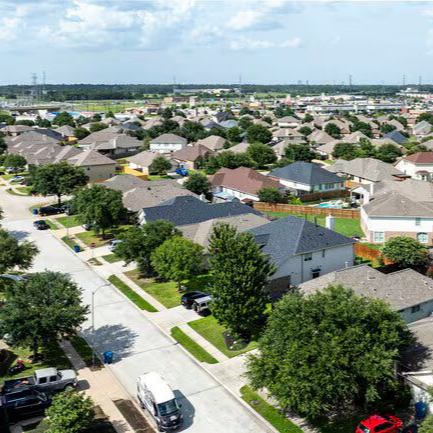 Aerial view of a suburban neighborhood with rows of houses, tree-lined streets, and a distant skyline.