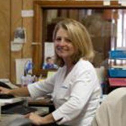Woman with blonde hair working at a desk, smiling, in an office setting.
