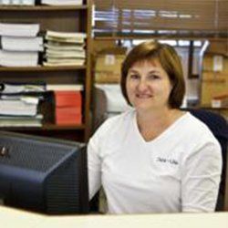Woman with brown hair smiles, working at a computer in an office setting.
