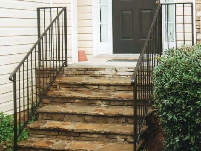 A set of stone stairs with a metal railing leading up to the front door of a house