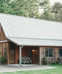 White siding building with French doors and two small square windows, set against a background of trees.