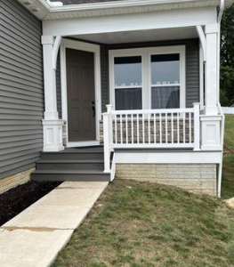 A grey house with a covered porch, white columns and railing, grey stairs, and a dark brown front door.