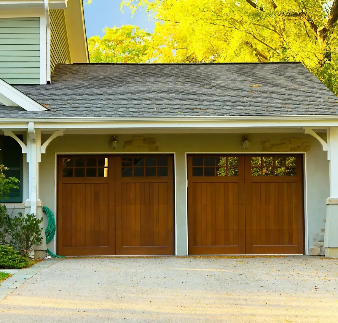 A row of three townhomes with brick and stucco facades, garage doors, and driveways on a sunny day.