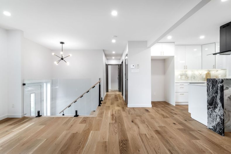 Bright, modern interior with hardwood floors. Open-concept kitchen and staircase, featuring white walls, cabinets and countertop.