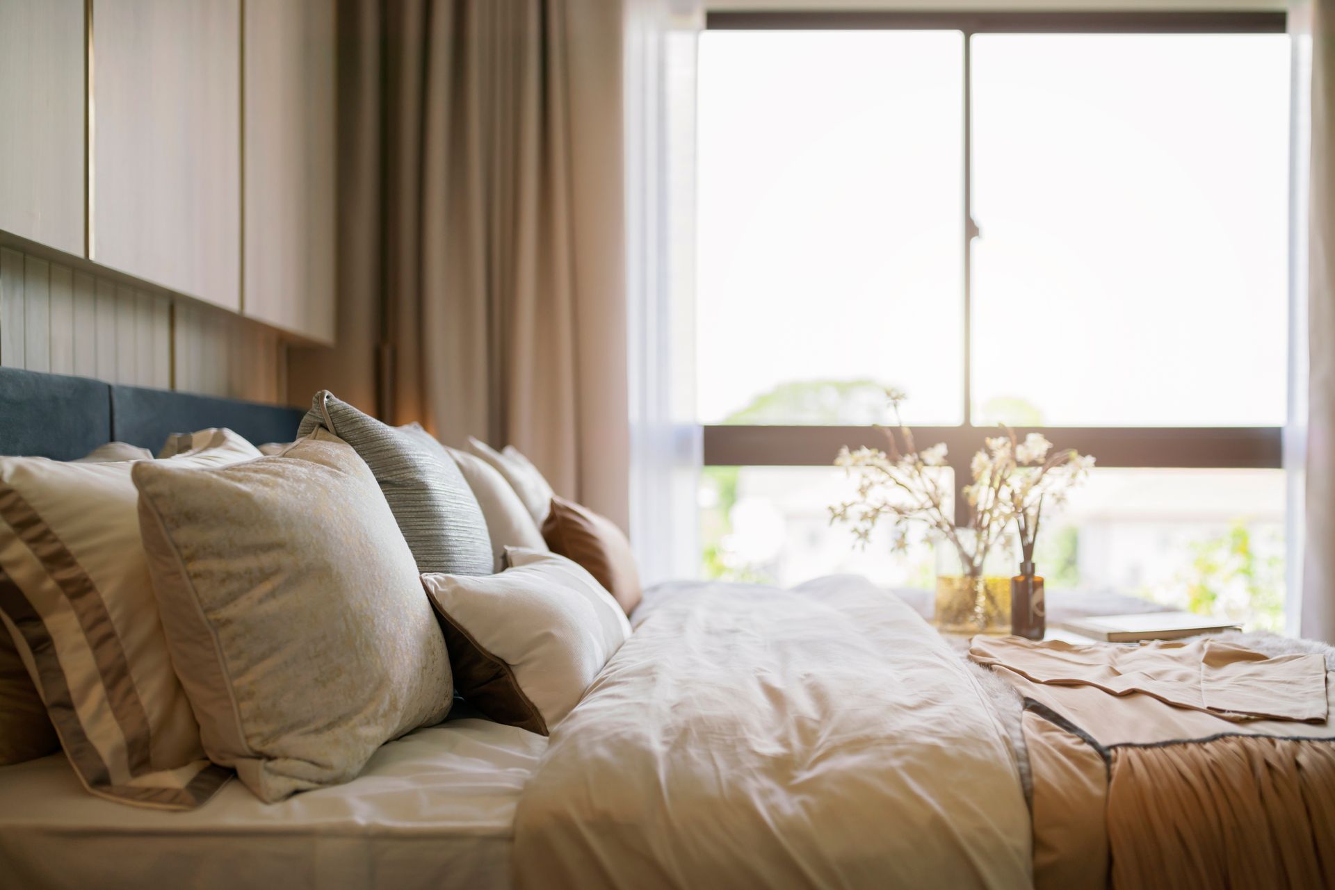 A cozy guest bedroom with a window in the background featuring layered custom drapery
