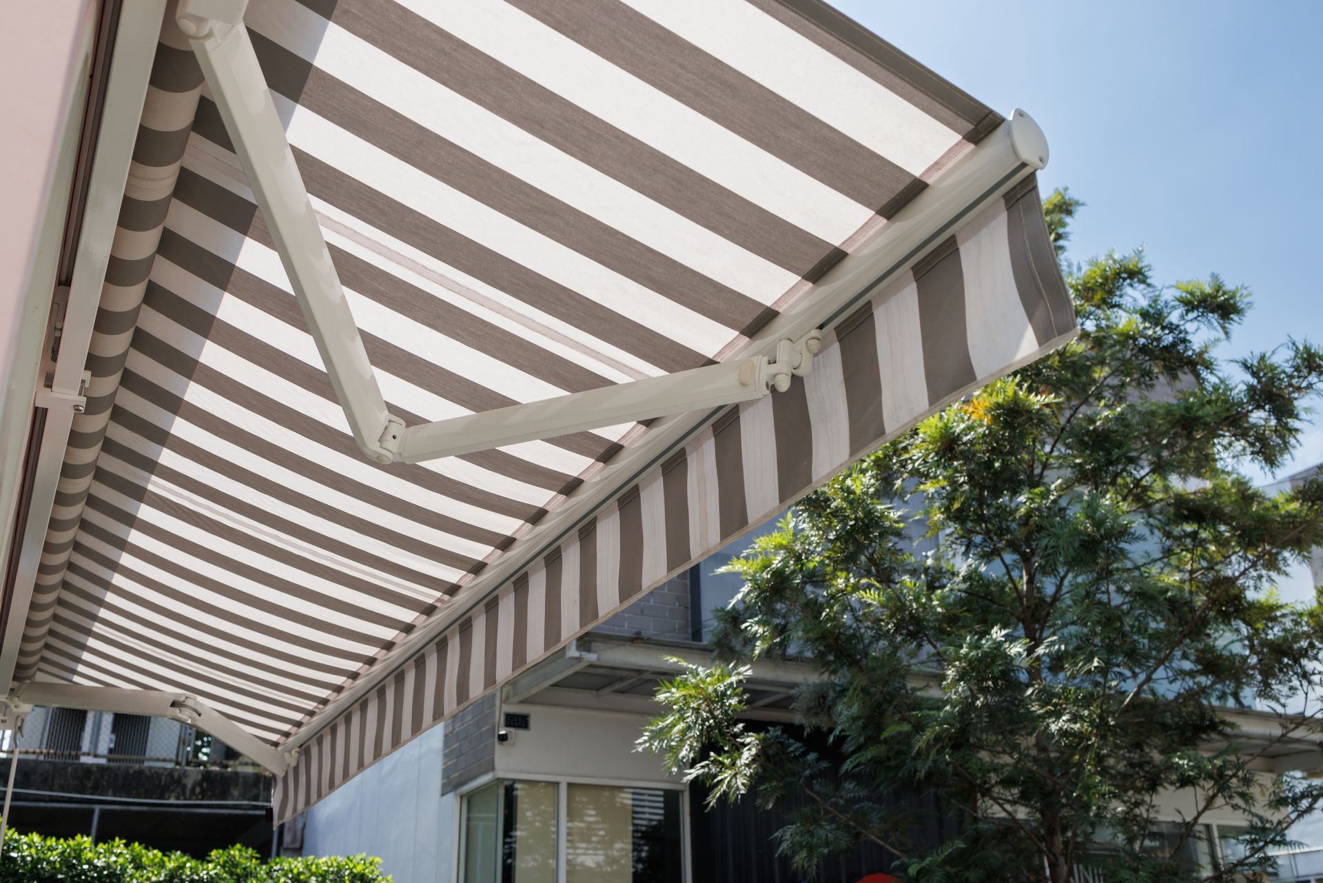A white and gray striped backyard awning, attached and opening from a home's exterior