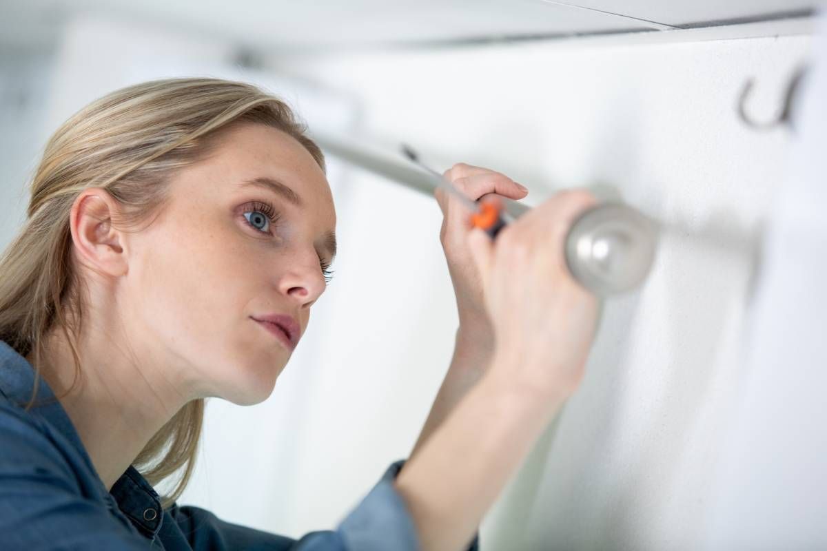 Blonde woman hanging a rod for custom drapes with grommets, rod pockets, tabs, or pleats near Lewiston & Moscow, ID and Clarkston & Pullman, WA