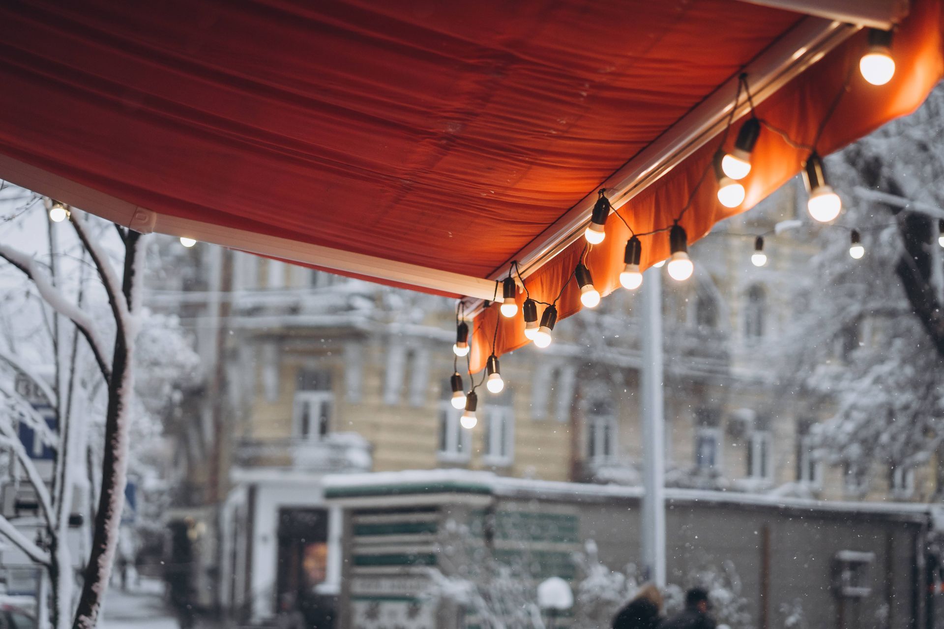 A red awning with string lights extended to the open position during a snowy winter day at The Blind Guy Lewiston near Clarkston & Pullman, WA