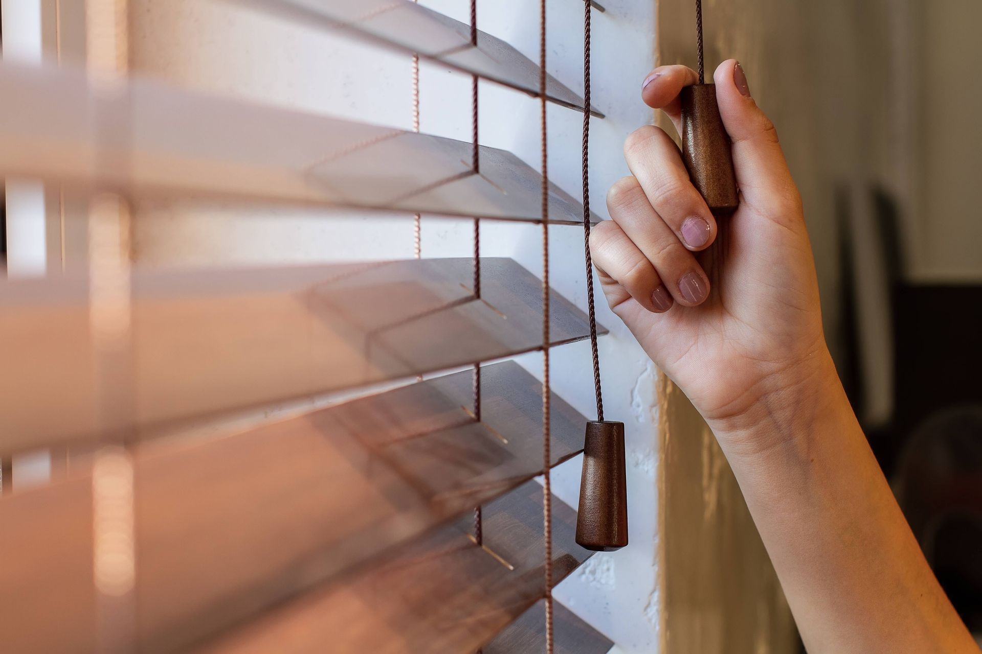 A woman's hand using a cord to open the best blinds for a home at The Blind Guy Lewiston near Clarks