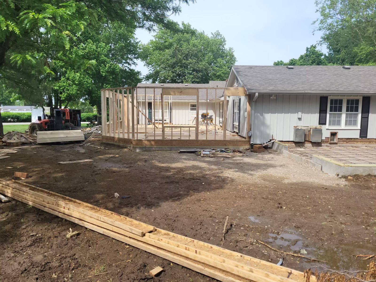 Construction site house undergoing renovation. Wooden framing is partially built; the yard is muddy with construction debris.