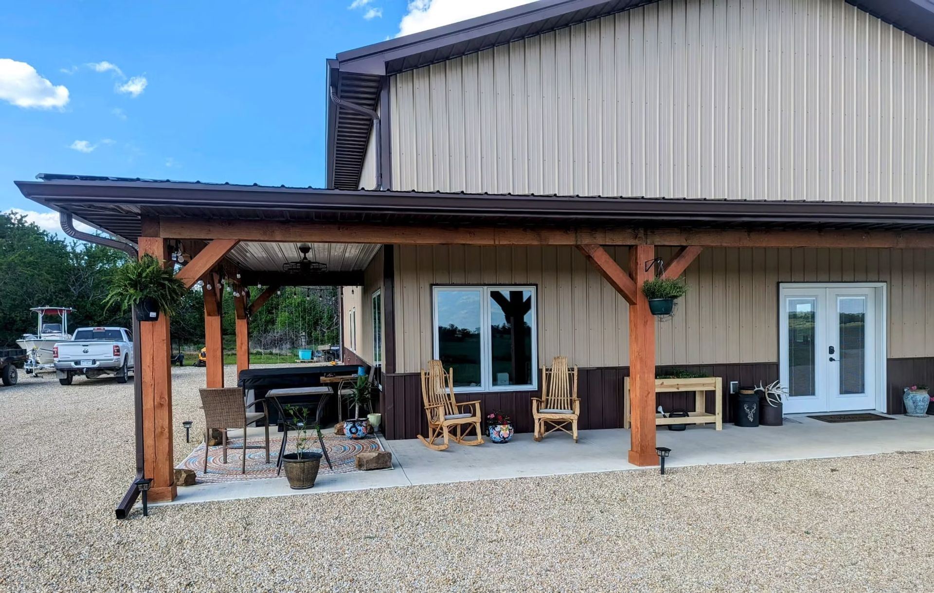 A tan building with a brown awning and patio.  The patio has seatgravel driveway.