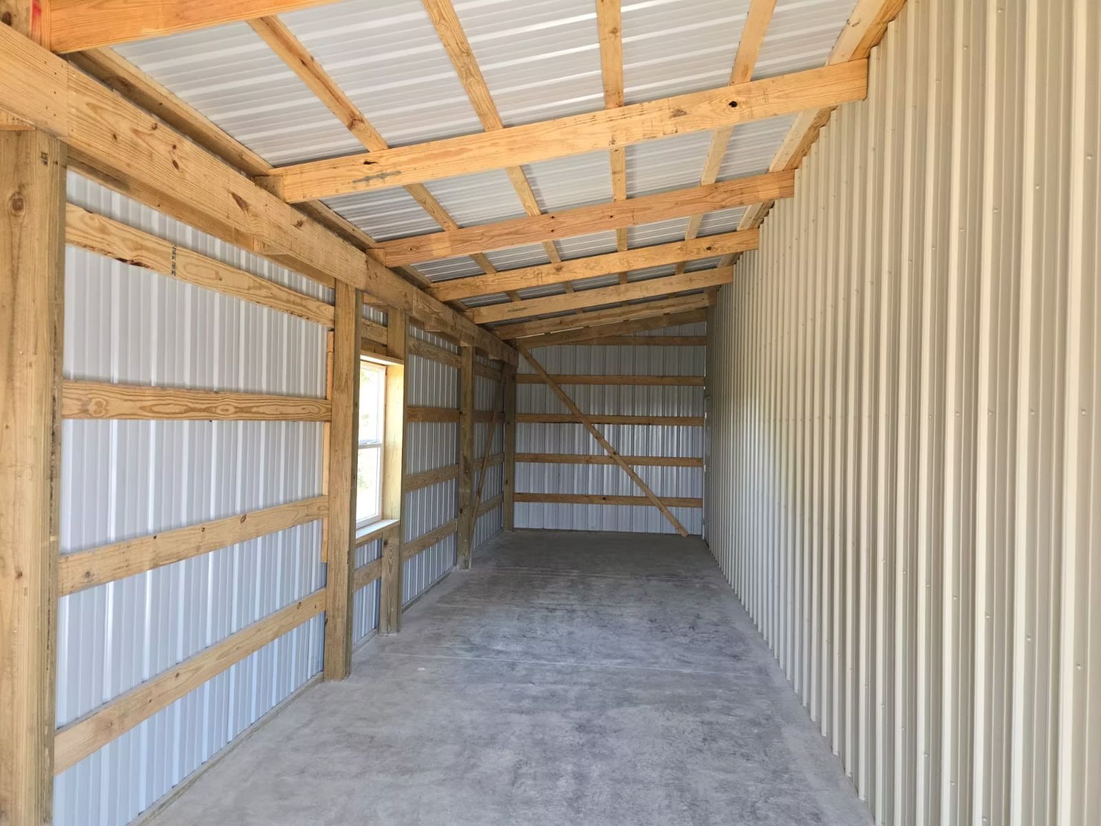 Interior view of a newly constructed metal building. Wooden framng supports the metal siding and roof, with a concrete floor.