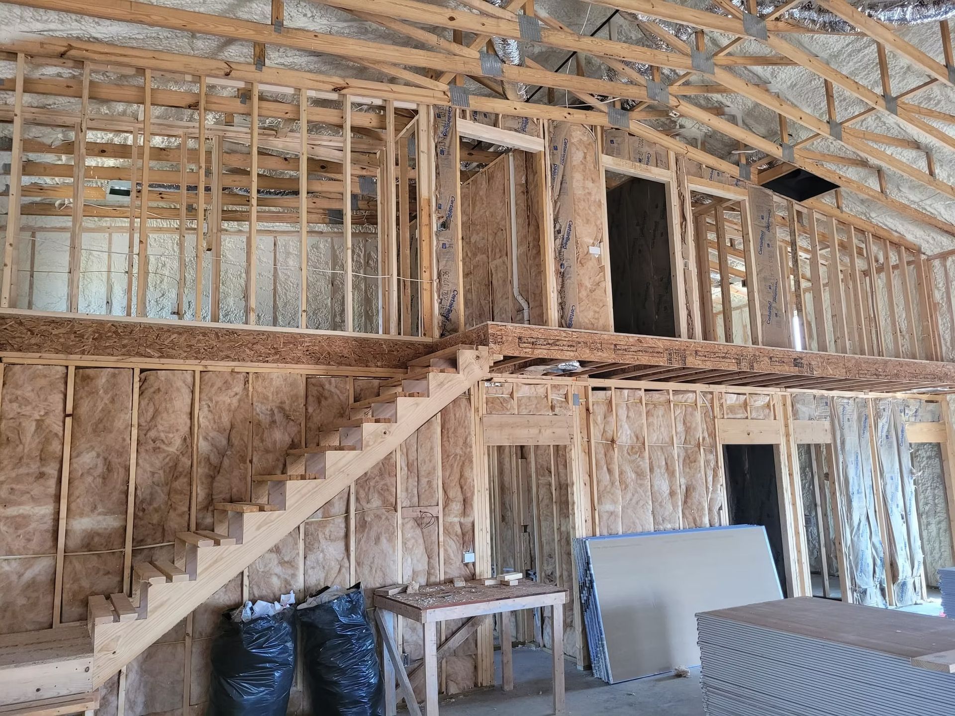 Interior of a bruction, showing wooden framing, a staircase, and exposed insulation. A partial second-story loft is visible.