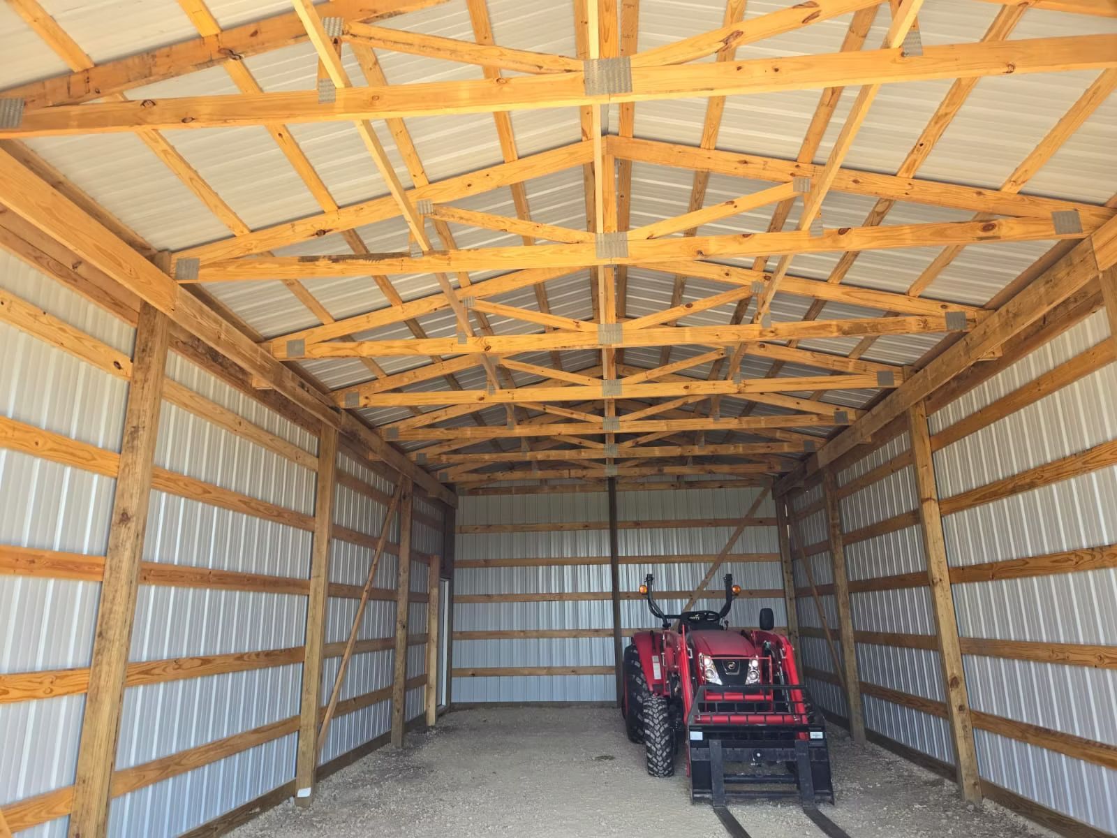 Inside a newly-built bae through the open doorway. The barn is constructed with wood beams and white metal siding.