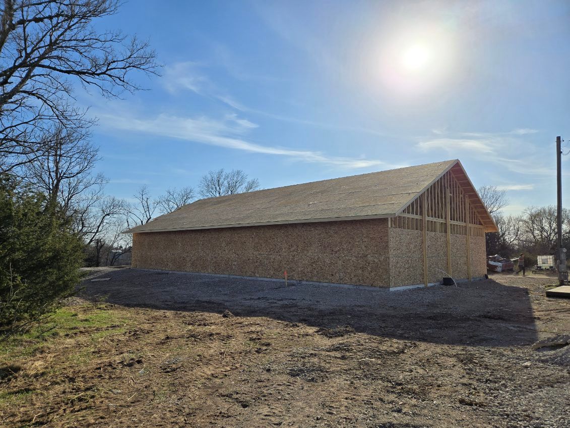 Brick barn with a metal roof in a rural field under a bright sun and blue sky