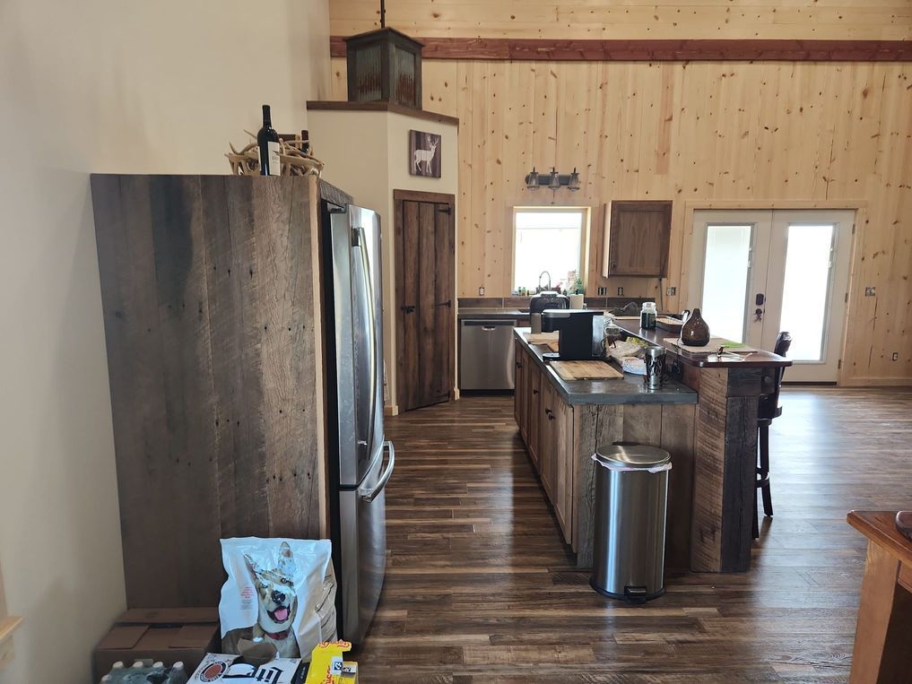 A rustic, modern kitchen with wood-paneled walls, dark wood cabinets, stainless appliances, and an island with a trash can.