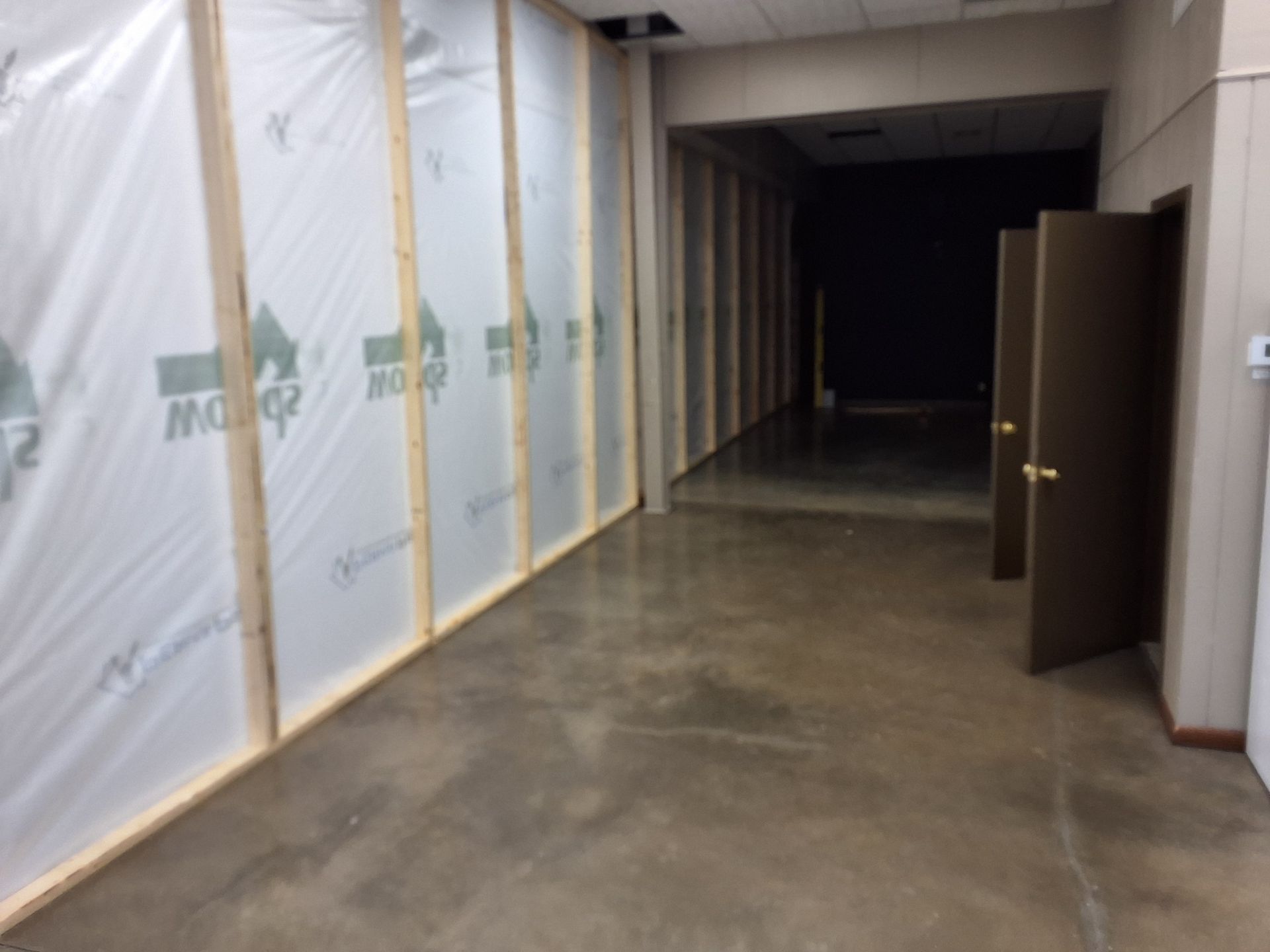 Construction area with a wooden frame wall covered in plastic sheeting next to an open doorway leading to a dark room.