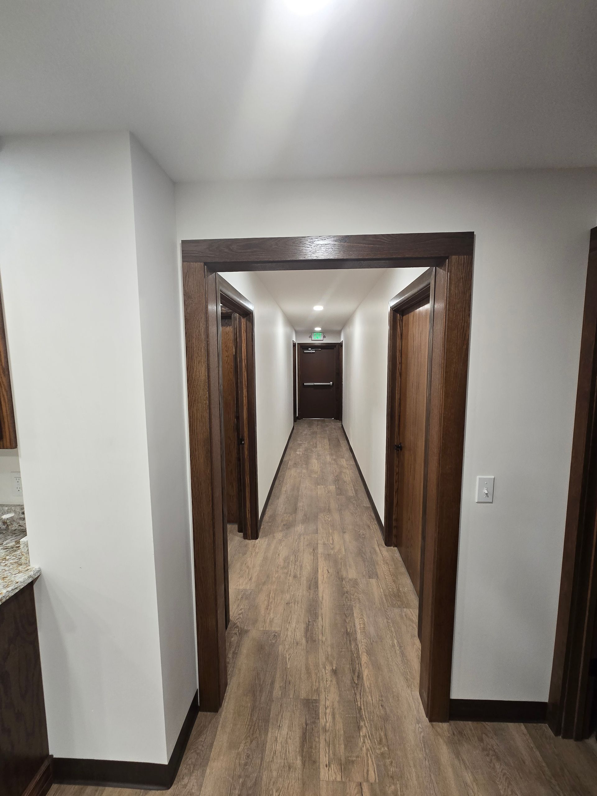 A view looking down a narrow hallway with wood-toned doors and flooring, framed by a dark wooden doorway in the foreground.