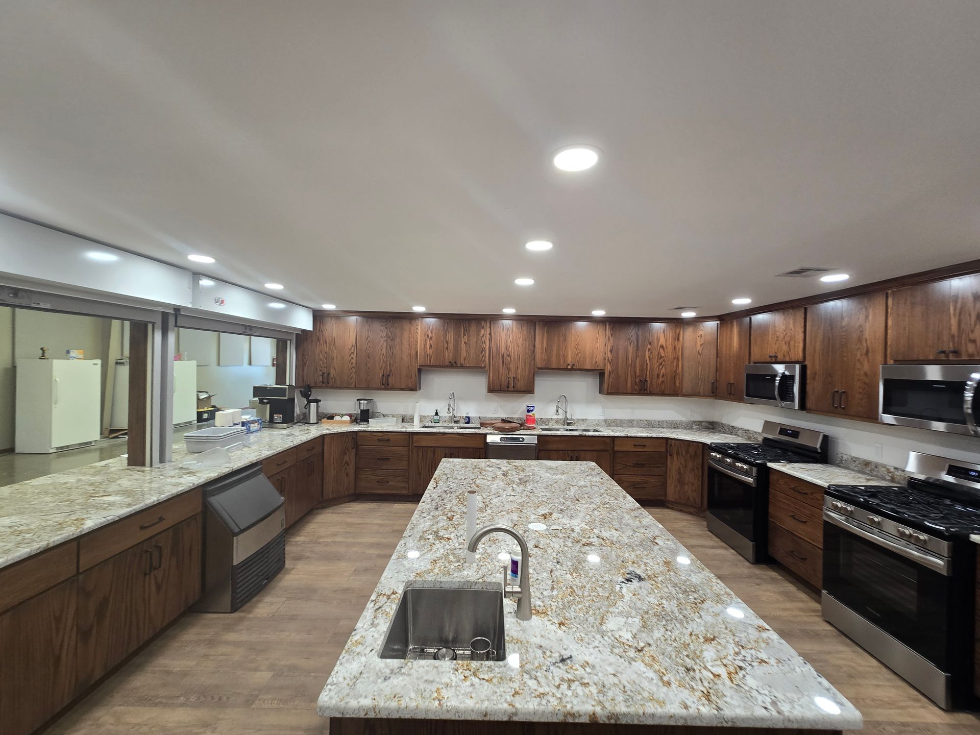 A kitchen featuring dark wood cabinets, light granite countertops, a large center island.