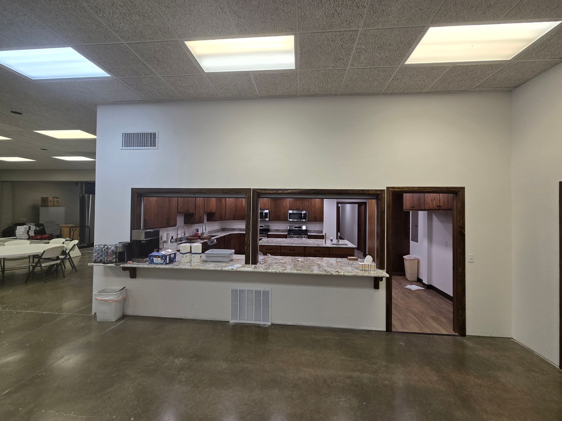 A room with a polished concrete floor, a service window opening into a kitchen, and an adjacent doorway.