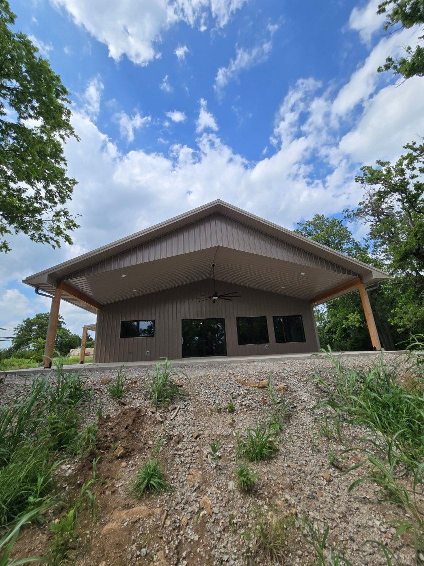 Rural house with a sloped roof on a hill, surrounded by trees under a partly cloudy sky.