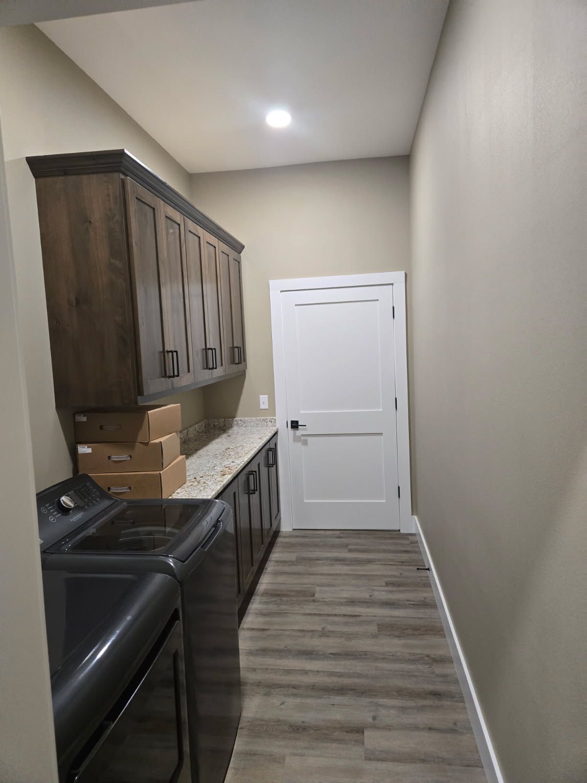 Narrow kitchen with dark wood cabinets, black appliances, and a white door at the end.