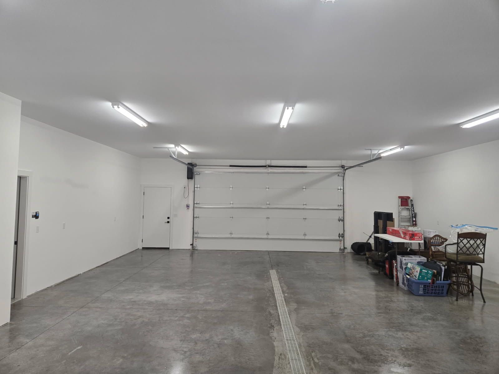 Empty two-car garage with white walls, closed garage door, and storage items along the right side.