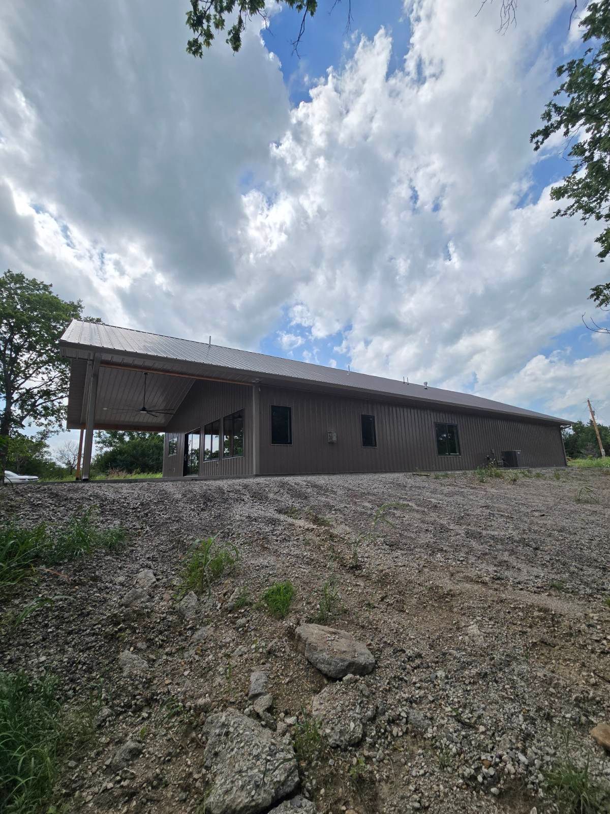 Single-story gray building on a rocky hillside beneath a cloudy blue sky